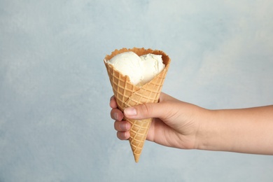 Woman holding delicious ice cream in wafer cone on light blue background, closeup