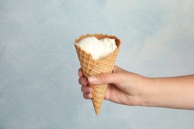 Photo of Woman holding delicious ice cream in wafer cone on light blue background, closeup