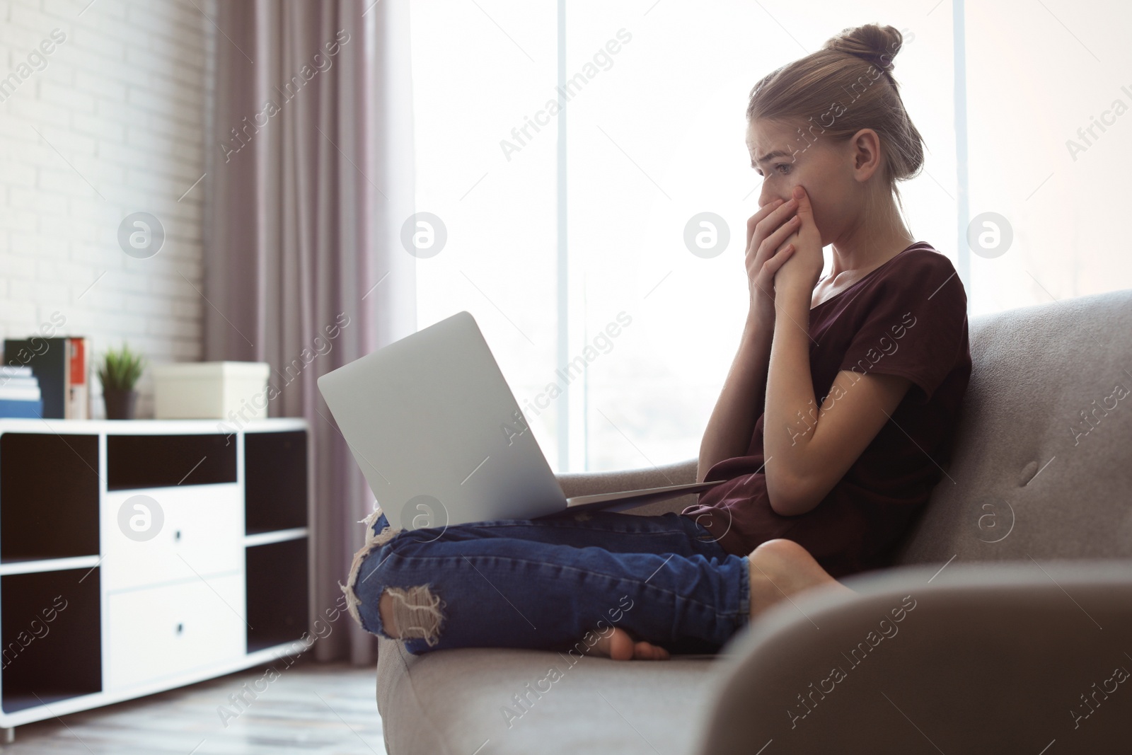 Photo of Shocked teenage girl with laptop in room. Danger of internet