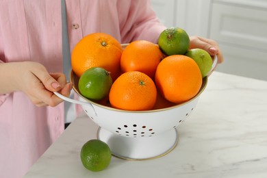 Photo of Woman holding colander with fresh fruits at white marble table, closeup