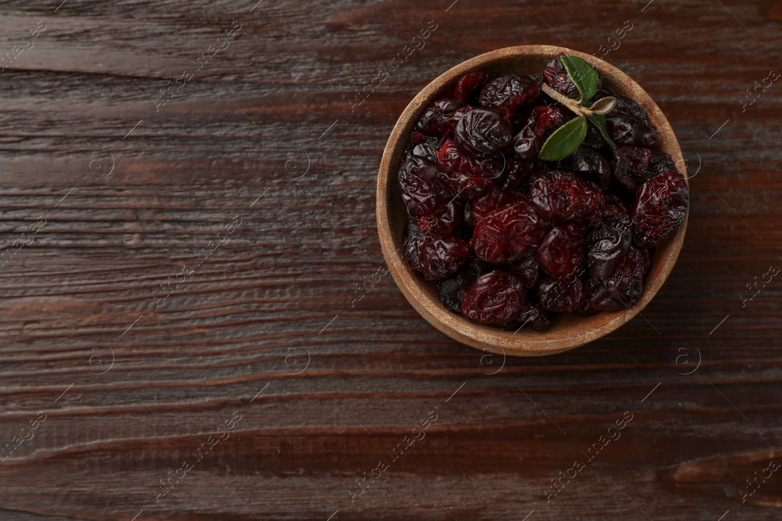 Photo of Tasty dried cranberries in bowl on wooden table, top view. Space for text