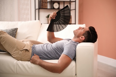 Photo of Man with hand fan lying on sofa. Summer season