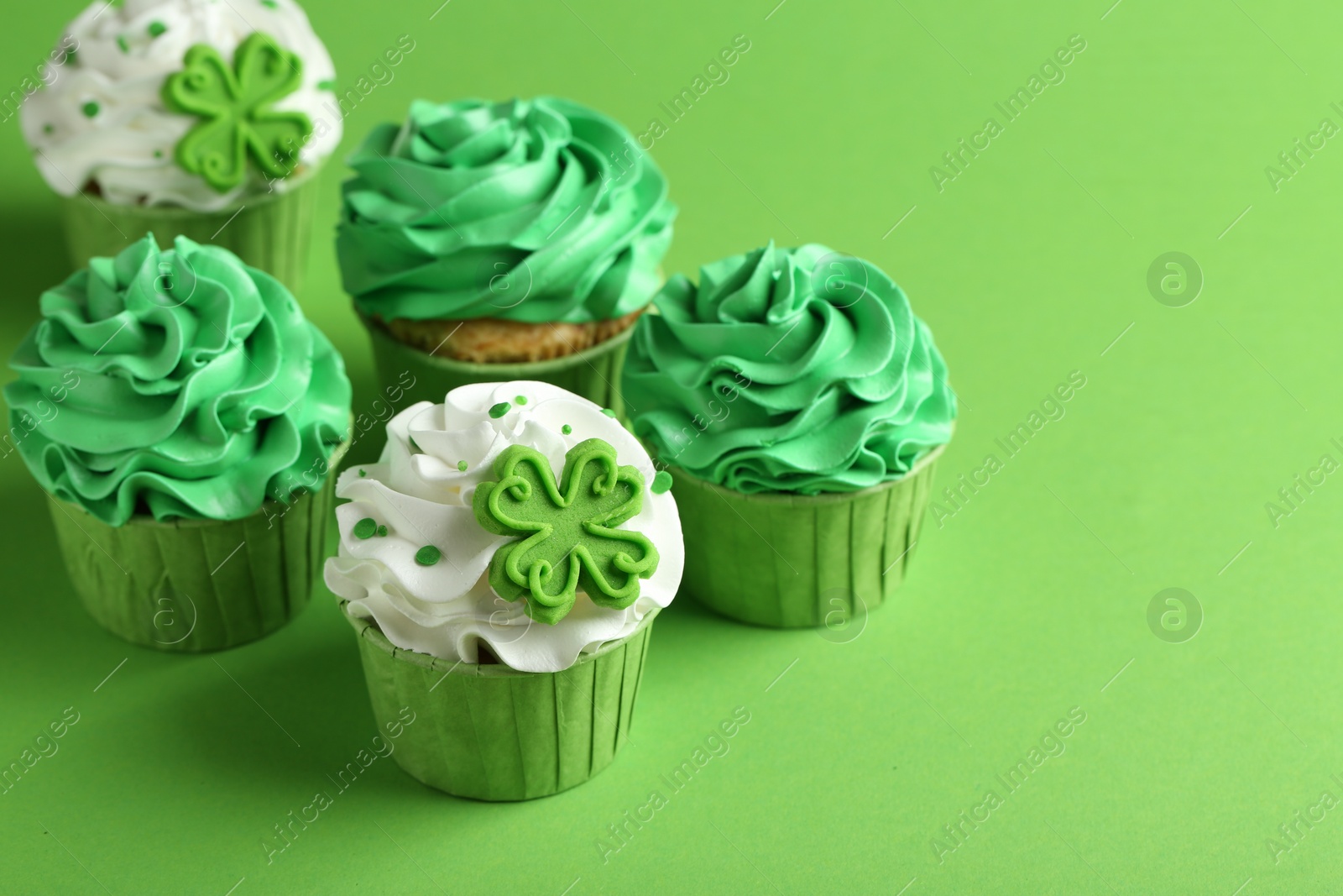 Photo of St. Patrick's day party. Tasty festively decorated cupcakes on green background, closeup. Space for text