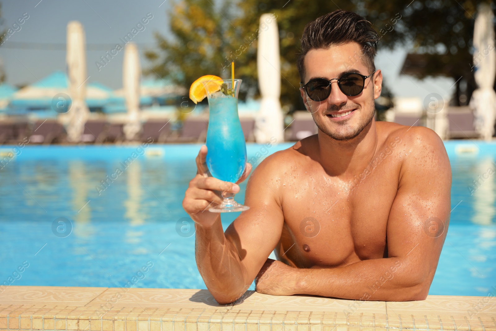 Photo of Young man with cocktail in pool on sunny day