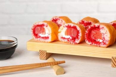 Photo of Delicious sushi rolls with salmon, chopsticks and soy sauce on white wooden table