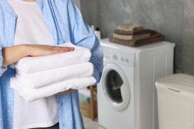 Photo of Woman holding folded soft terry towels in bathroom, closeup. Space for text