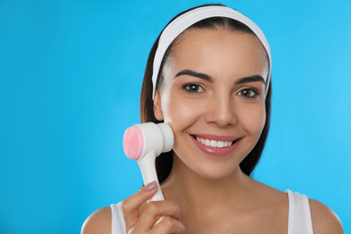 Photo of Young woman using facial cleansing brush on light blue background. Washing accessory