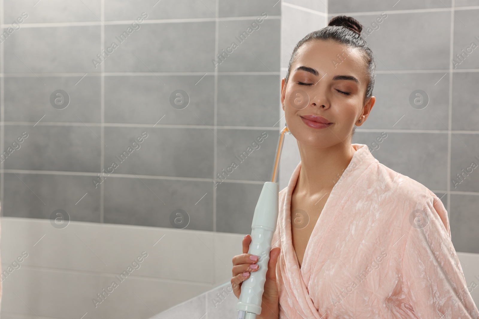 Photo of Woman using high frequency darsonval device in bathroom, space for text