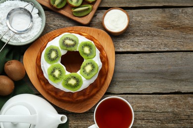 Photo of Homemade yogurt cake with kiwi, cream and aromatic tea on wooden table, flat lay. Space for text