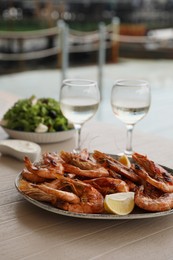 Photo of Plate of delicious cooked shrimps served with lemon and wine at table outdoors