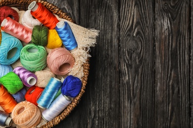 Basket with color sewing threads on wooden background, top view