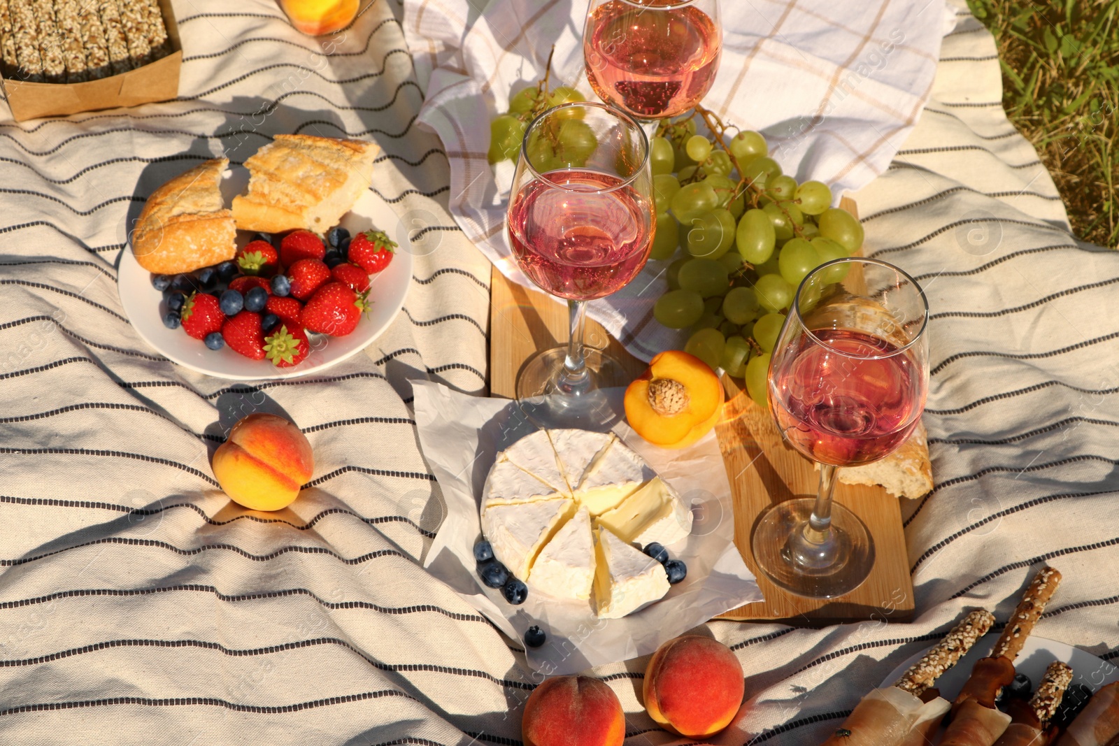 Photo of Glasses of delicious rose wine and food on picnic blanket outdoors