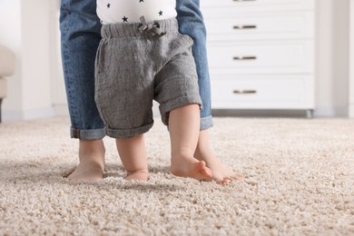Photo of Mother supporting her baby son while he learning to walk on carpet at home, closeup. Space for text
