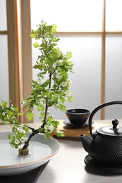 Stylish ikebana as house decor. Beautiful fresh branch and tea set on wooden table