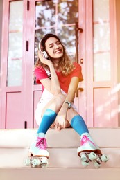 Image of Happy girl with retro roller sitting on stairs skates near pink door