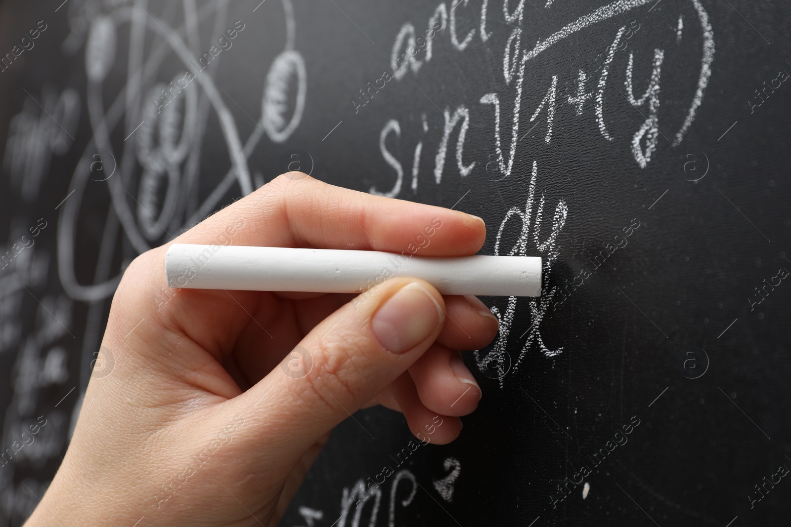 Photo of Teacher writing math formulas with chalk on blackboard, closeup