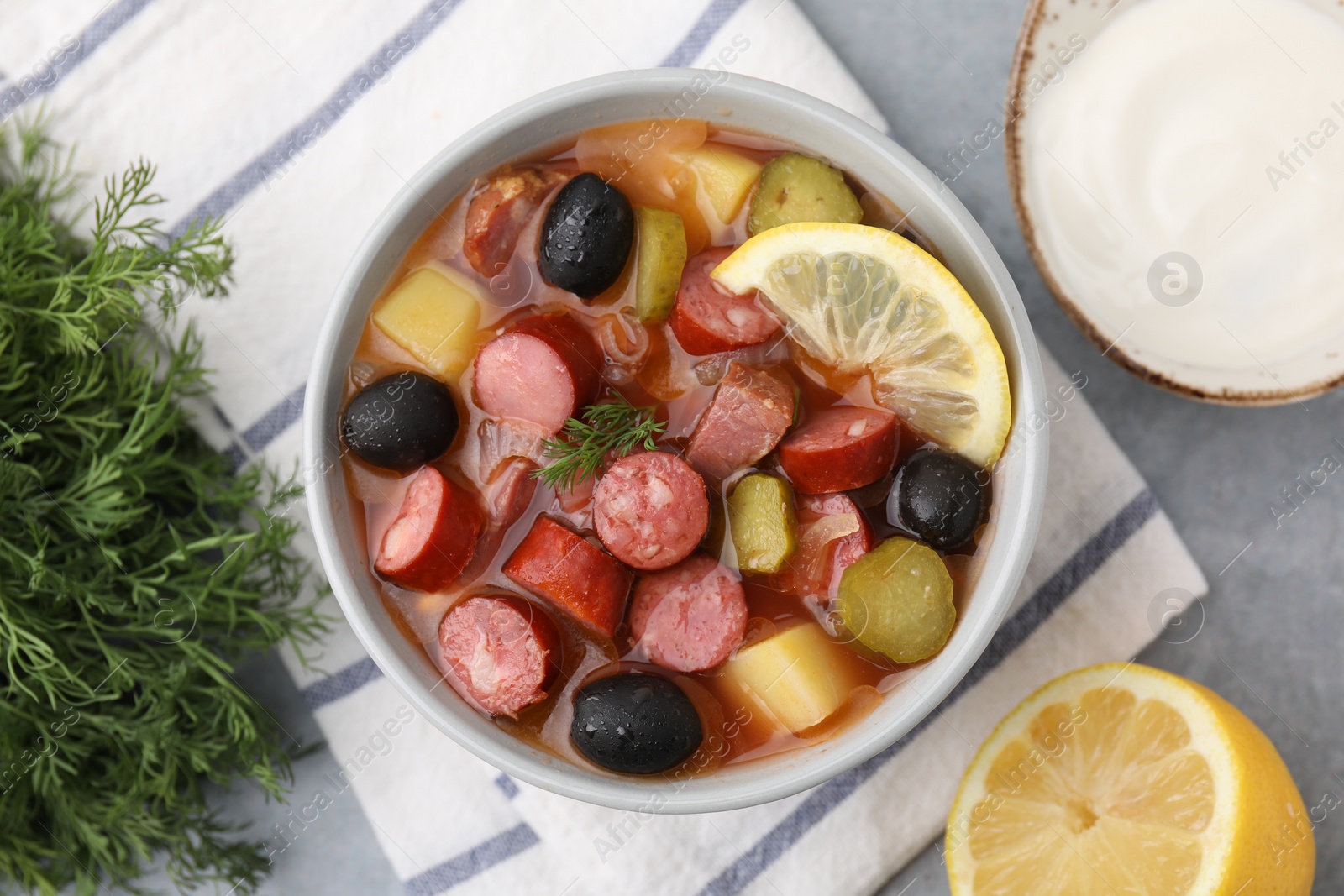 Photo of Meat solyanka soup with thin dry smoked sausages served on grey table, flat lay