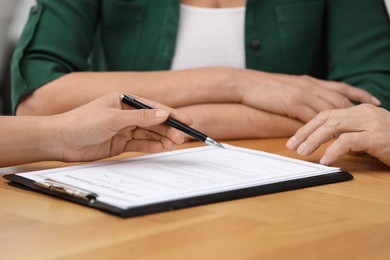 Notary showing senior couple where to sign Last Will and Testament at wooden table, closeup