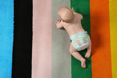 Cute little baby crawling on colorful carpet indoors, top view with space for text