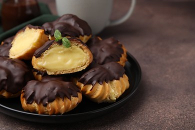 Photo of Delicious profiteroles with chocolate spread and cream on textured table, closeup. Space for text