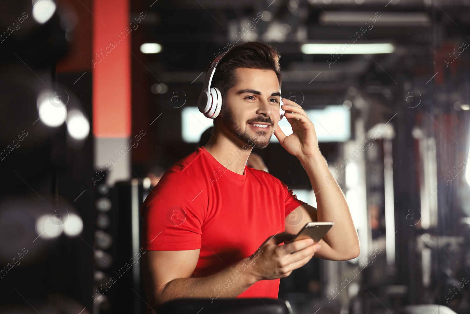 Photo of Young man with headphones listening to music on mobile device at gym