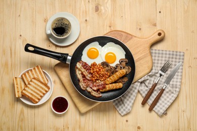 Frying pan with cooked traditional English breakfast and cup of coffee on wooden table, flat lay