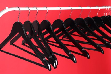 Photo of Black clothes hangers on metal rack against color background, closeup view