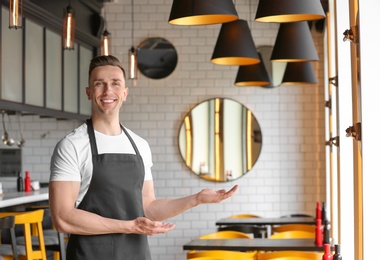 Photo of Portrait of young waiter in uniform at cafe