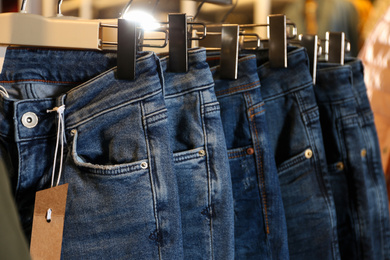 Photo of Modern jeans hanging on clothing rack in shop, closeup