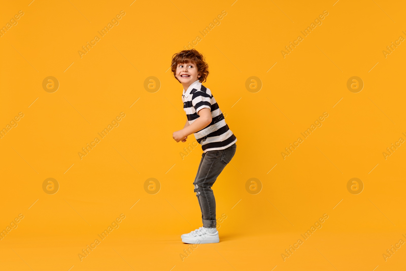 Photo of Happy little boy dancing on yellow background. Space for text