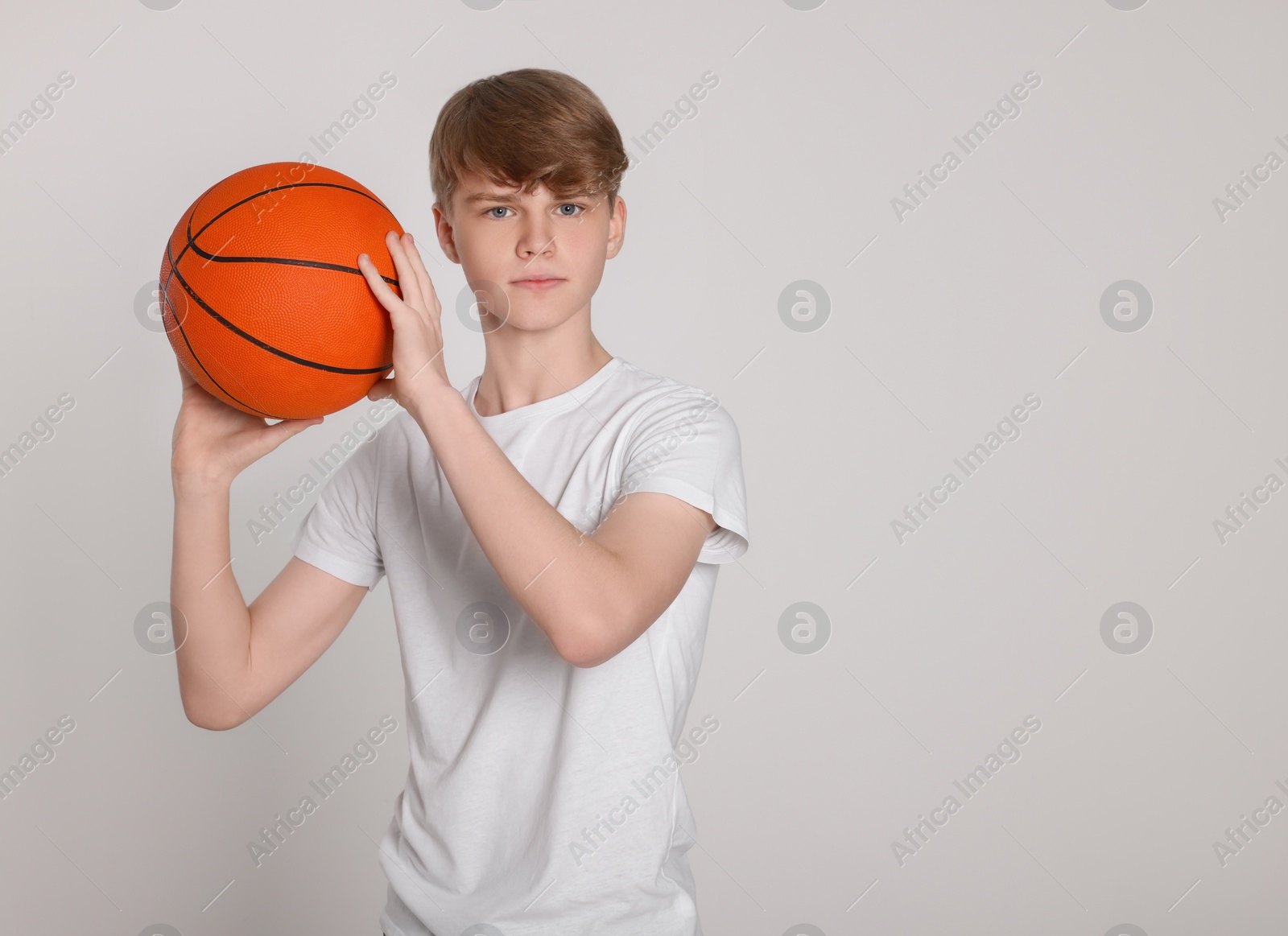 Photo of Teenage boy with basketball ball on light grey background. Space for text