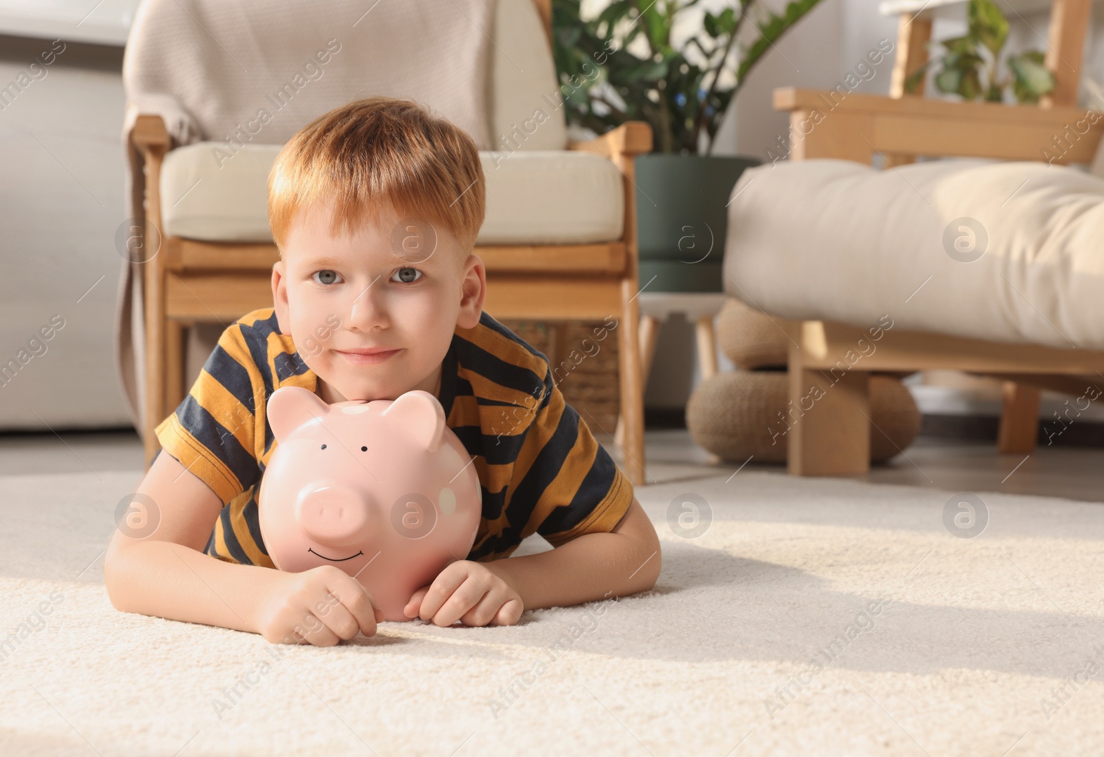 Photo of Cute little boy with ceramic piggy bank on floor at home