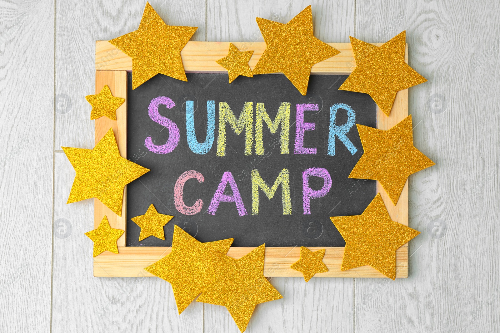 Photo of Decorated blackboard with text SUMMER CAMP chalked in different colors on wooden background, top view