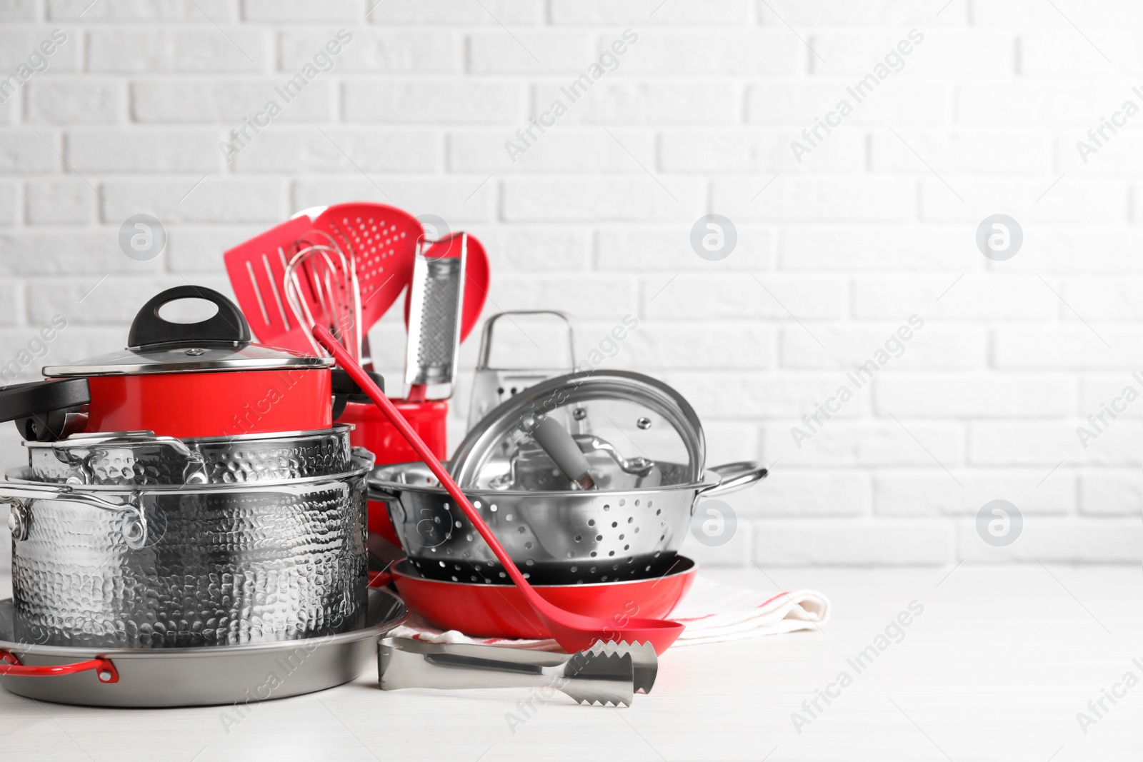 Photo of Set of clean kitchenware on white table against brick wall. Space for text