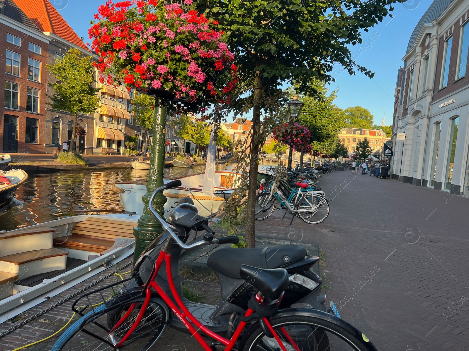 Photo of Leiden, Netherlands - August 1, 2022: Picturesque view of city canal with moored boats and parked bicycles