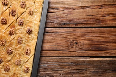 Photo of Delicious baklava with walnuts in baking pan on wooden table, top view. Space for text