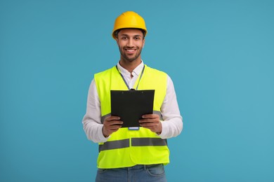 Engineer in hard hat holding clipboard on light blue background