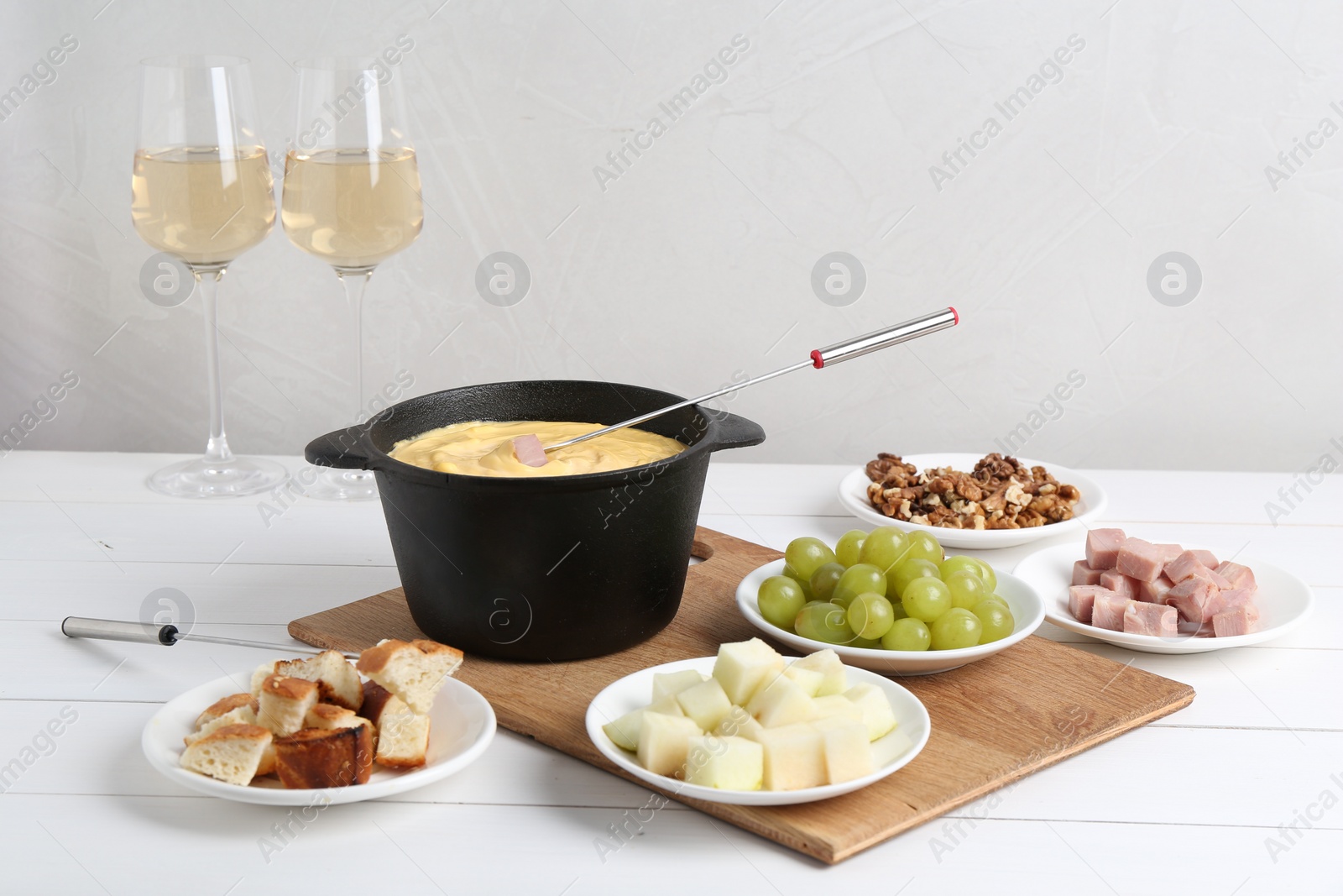 Photo of Fondue pot with tasty melted cheese, forks, wine and different snacks on white wooden table