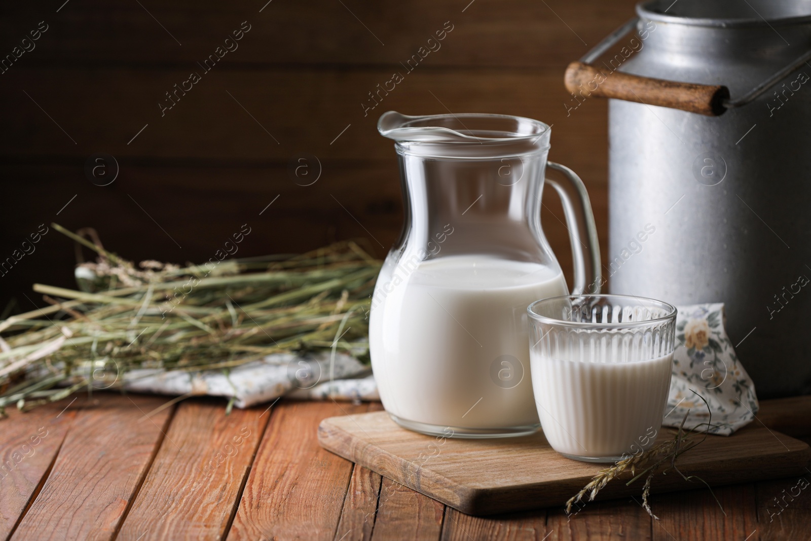 Photo of Tasty fresh milk in can, jug and glass on wooden table. Space for text