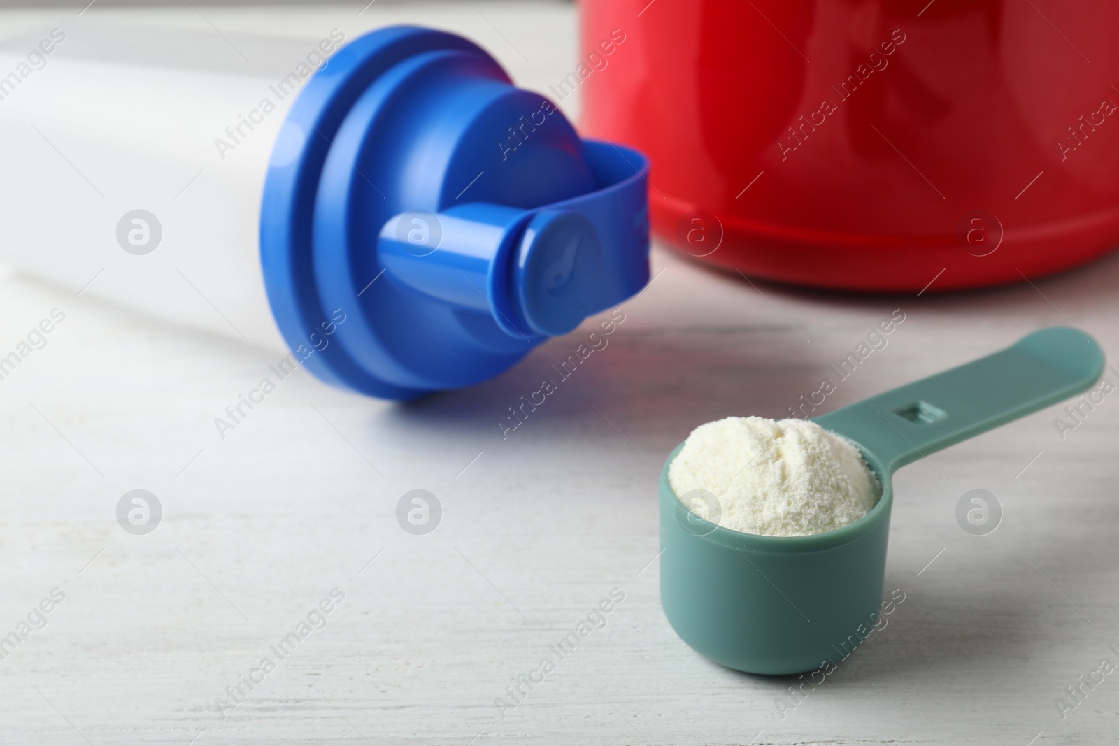 Photo of Scoop of protein powder and sports bottle on white wooden table, space for text