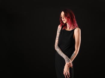 Beautiful woman with tattoos on arms against black background. Space for text