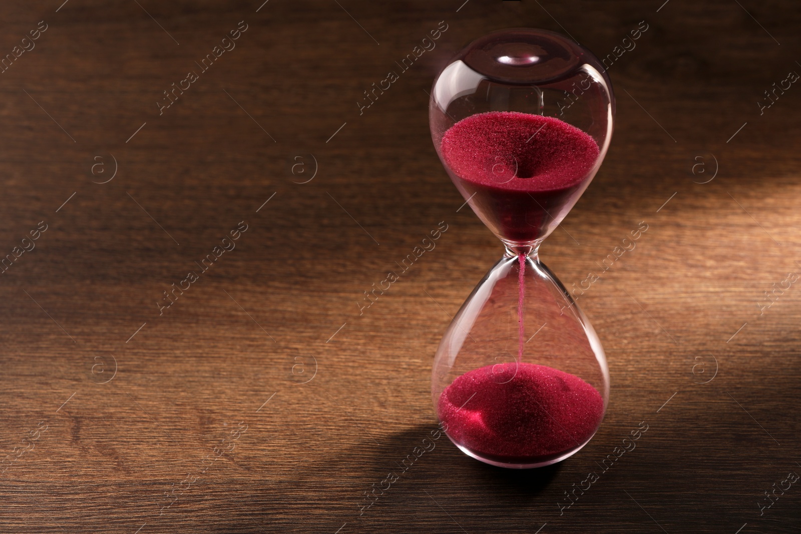 Photo of Hourglass with pink flowing sand on wooden table. Space for text