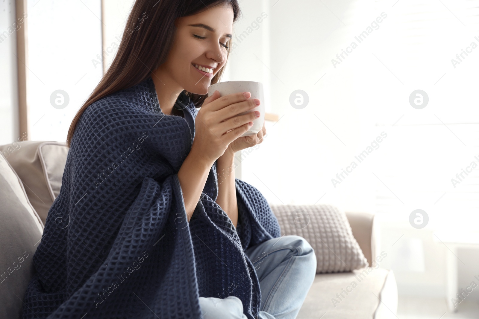 Photo of Woman covered with warm dark blue plaid enjoying hot drink on sofa at home