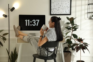 Photo of Young woman with cup of tea at table in light room. Home office