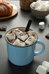 Photo of Delicious hot chocolate with marshmallows, cocoa powder and spoon on grey table, closeup