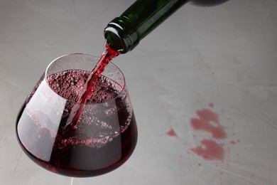 Photo of Pouring tasty red wine in glass at gray table, closeup. Space for text