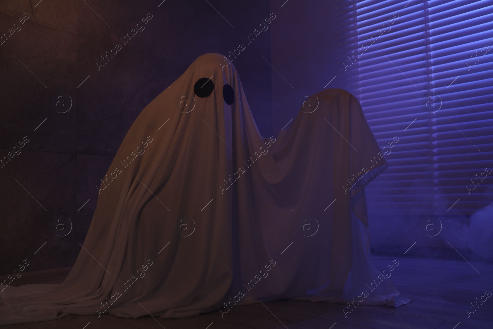 Photo of Creepy ghost. Woman covered with sheet near window in color lights