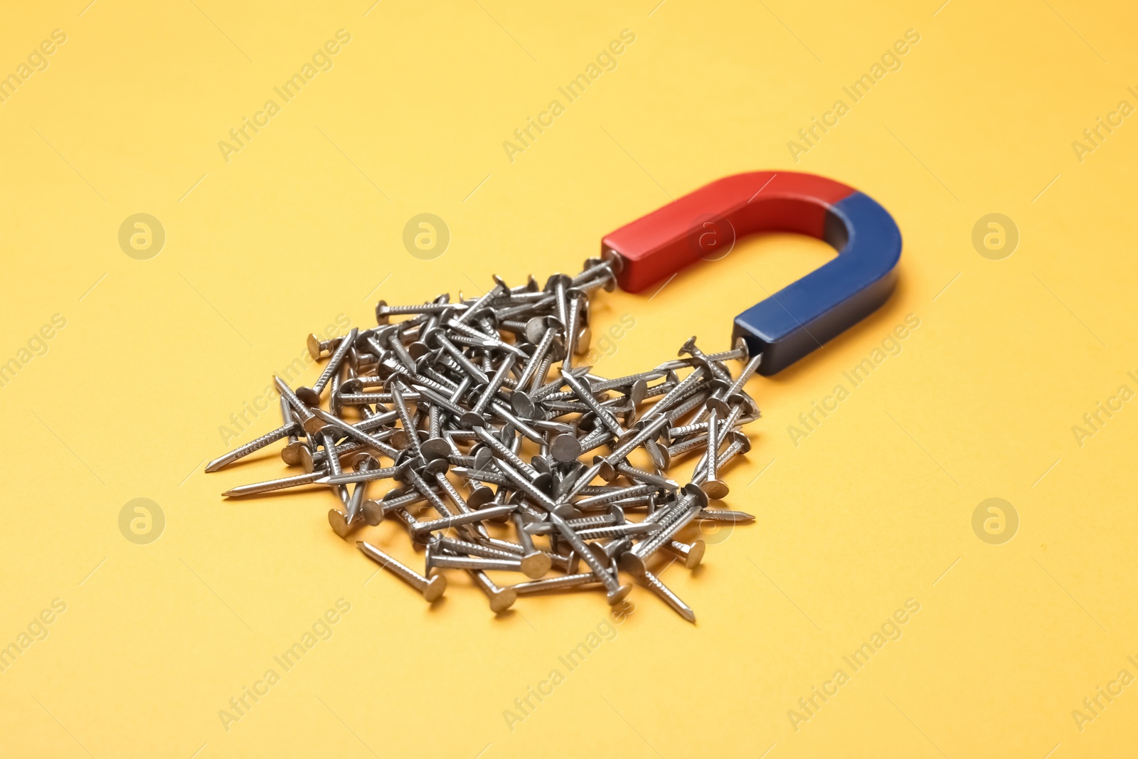 Photo of Horseshoe magnet attracting nails on color background
