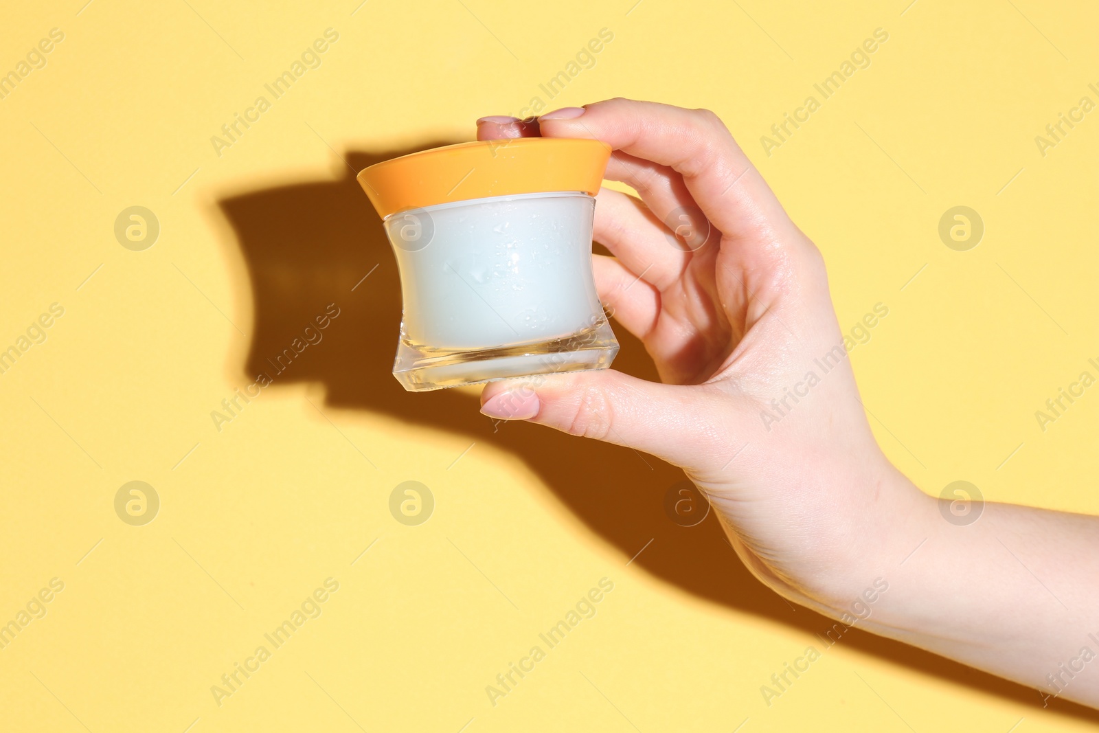 Photo of Woman holding jar of cream on yellow background, closeup