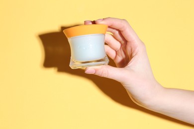 Woman holding jar of cream on yellow background, closeup